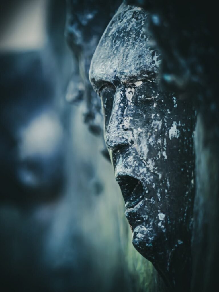 Moody close-up of a weathered stone face sculpture showing detailed textures.